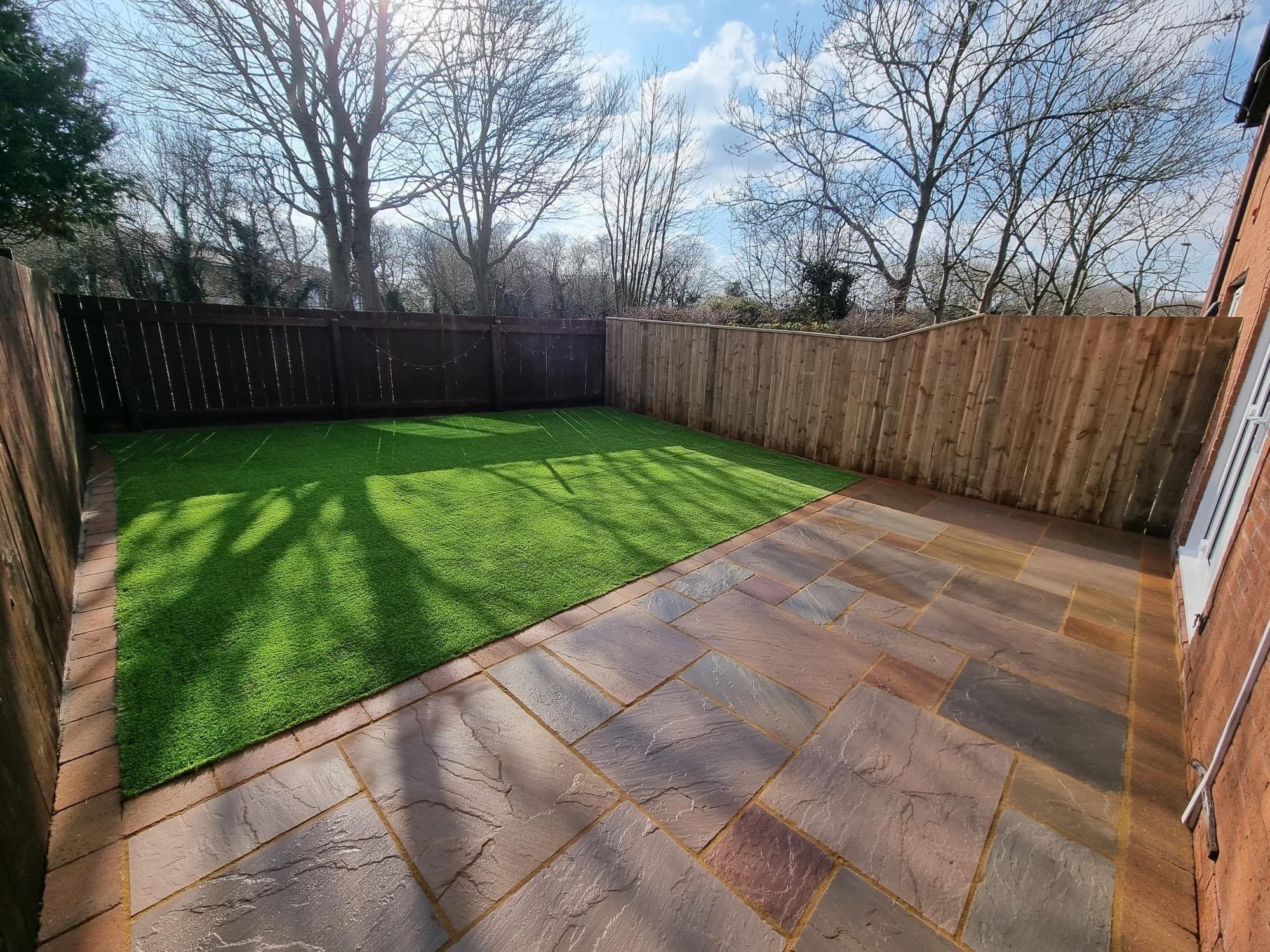Paved patio and artificial grass garden enclosed by timber fencing
