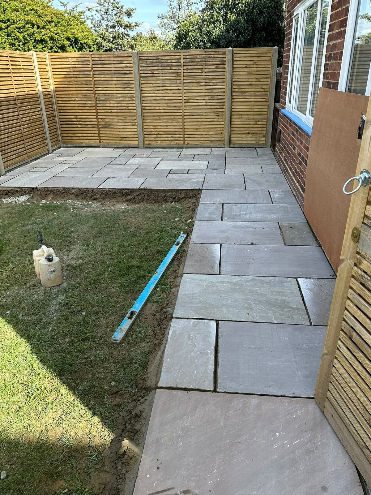 Grey sandstone patio slabs laid along a side return with slatted fencing
