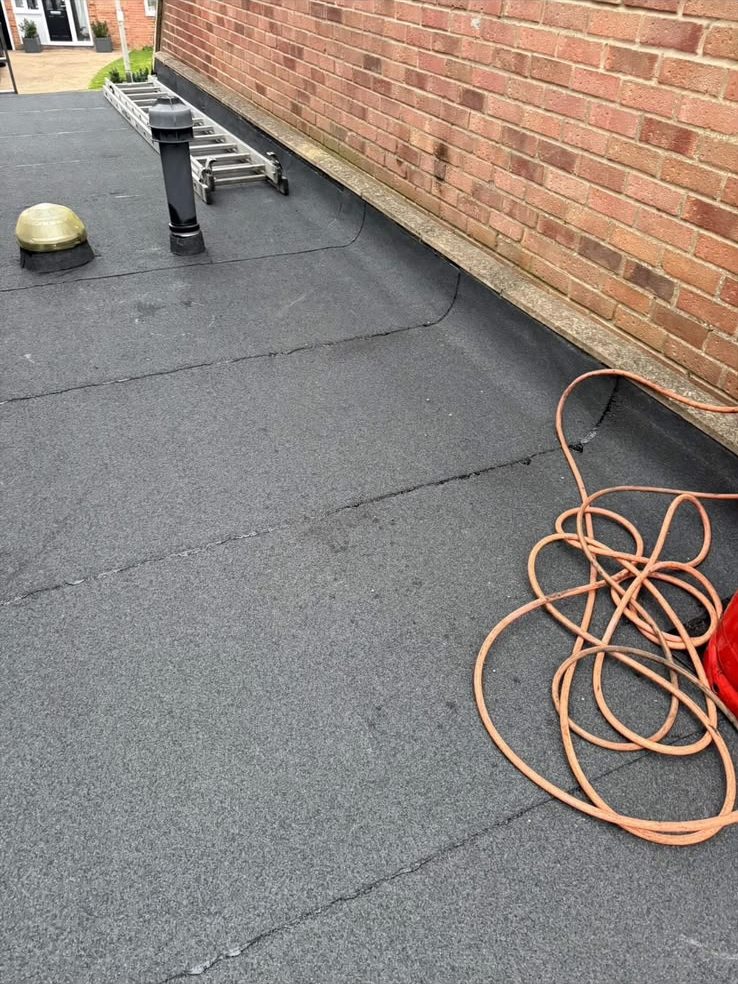 New felt flat roof installation with roof vent beside brick wall