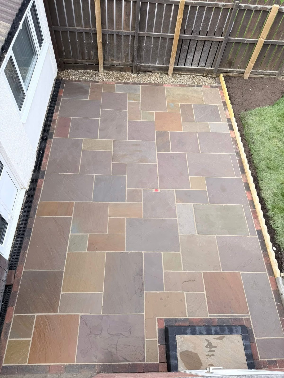 Indian sandstone patio laid beside a house with timber edging