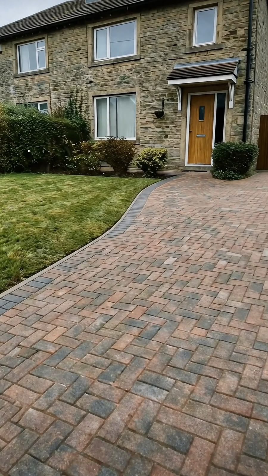 Curved herringbone block paving driveway leading to a stone house front door