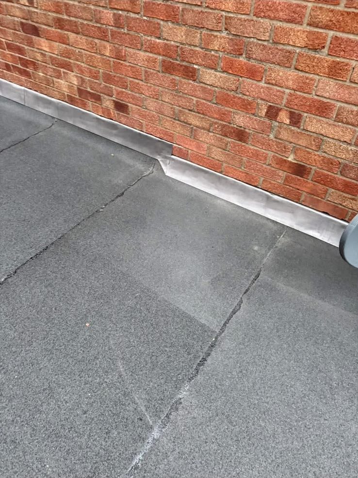 Lead flashing detail where a new felt flat roof meets brickwork