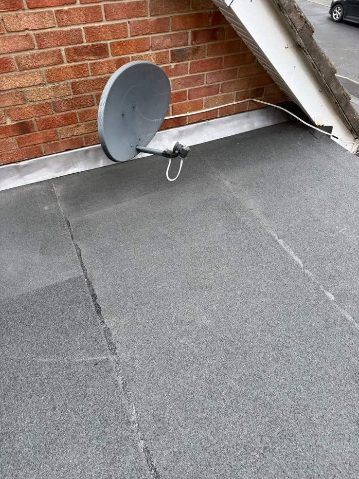 Newly installed mineral felt flat roof against a brick wall