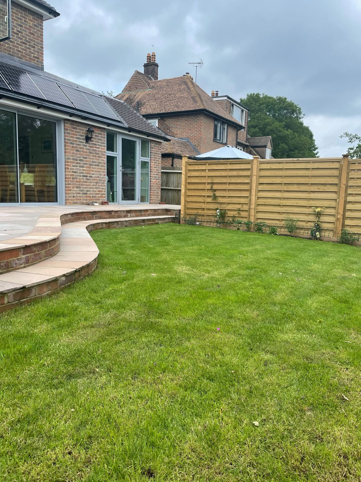 Raised curved sandstone patio with steps down to a new lawn